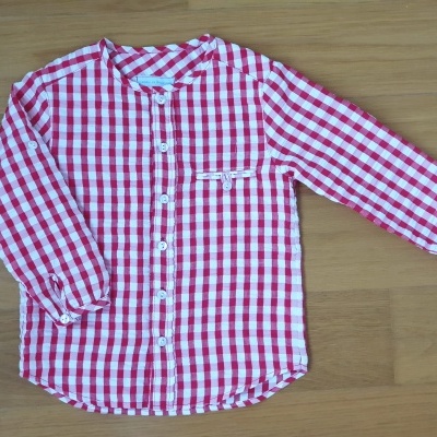 Camisa de criança vermelha e branca às quadrículas sobre superfície de madeira