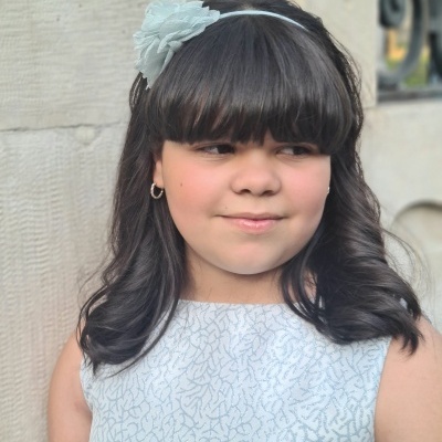Menina com faixa de cabelo branca com flor e vestido branco com padrão cinza