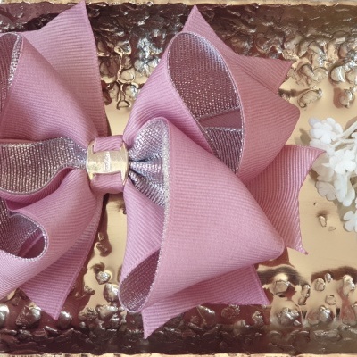Laço de cabelo rosa com fita prateada central numa superfície dourada com flores