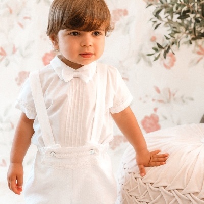 Criança com roupa branca num ambiente claro e decorado com flores e mobiliário trançado.