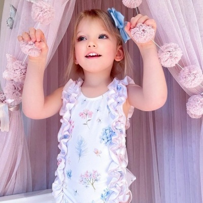 Menina com fato-de-banho floral branco com riscas rosas junto a cortinas e pompons cor-de-rosa