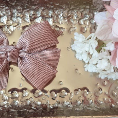 Laço castanho sobre bandeja dourada com flores rosas e brancas