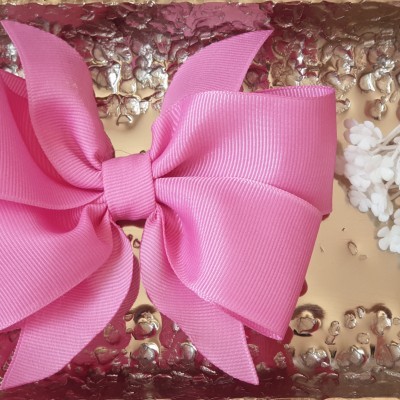 Laço de cabelo rosa sobre superfície metálica dourada com flores ao lado