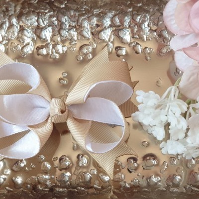 Laço em fita bege e branca sobre superfície metálica relvada com flores ao lado