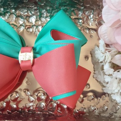 Laço de fita verde e rosa com aro metálico dourado sobre superfície metálica texturada e flores