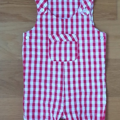 Macacão infantil xadrez vermelho e branco sobre madeira clara