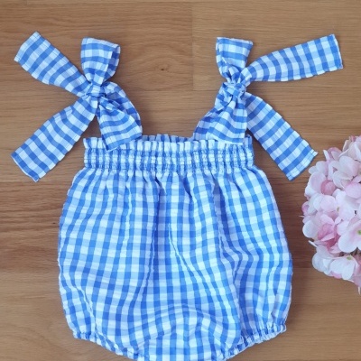 Body bebé azul e branco xadrez com alças laço sobre madeira