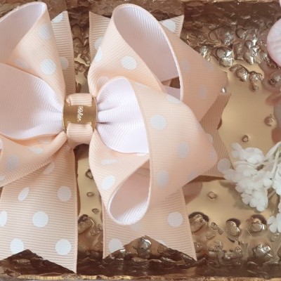 Laço decorativo rosa claro com bolinhas brancas sobre superfície metálica e flores