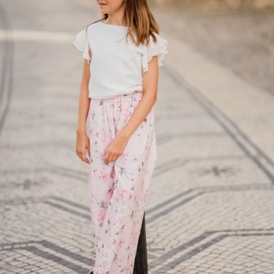 Rapazinha com blusa branca e calças rosa florais em calçada de mosaico português