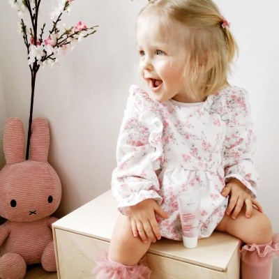 Menina com vestido floral rosa e branco sentada ao lado de brinquedo de coelho rosa