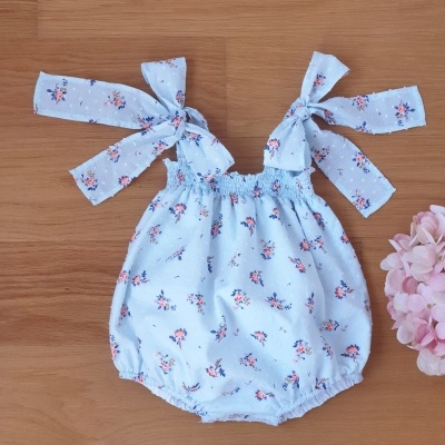 Macacão de bebé azul claro com padrão floral e alças com fitas.