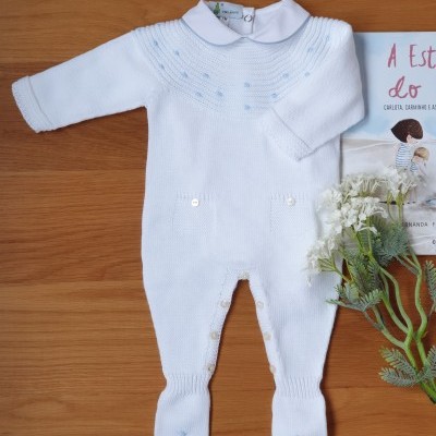 Macacão de bebé branco em malha com gola redonda e botões ao lado de livro e flores