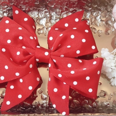 Laço vermelho com bolinhas brancas sobre superfície metálica prateada com flores ao lado