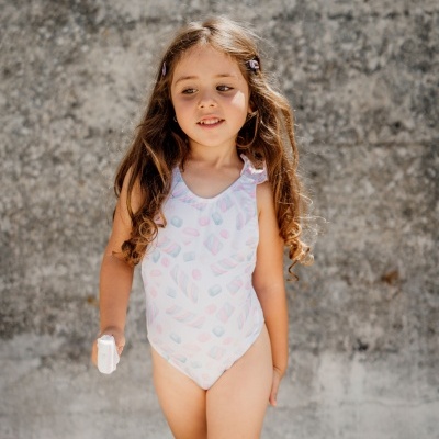 Menina a usar fato de banho branco com padrões coloridos e parede cinzenta atrás