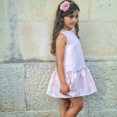 menina com vestido rosa claro e acessório de cabelo rosa em parede de pedra cinza