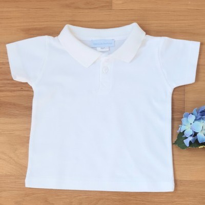 Camisola de criança tipo polo branca sobre superfície de madeira clara com flor azul ao lado