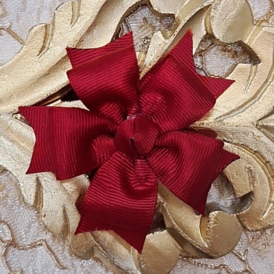 Laço vermelho de tecido com textura canelada sobre fundo de tecido bordado dourado e bege