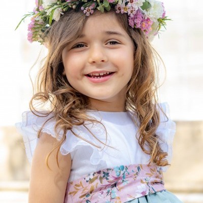 Criança com vestido azul e coroa de flores coloridas sorrindo