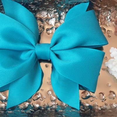 Laço azul em tecido sobre superfície prateada texturizada com flores ao lado