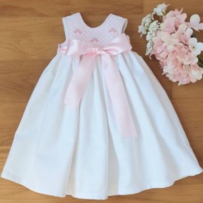 Vestido branco para bebé com laço rosa e flores ao lado