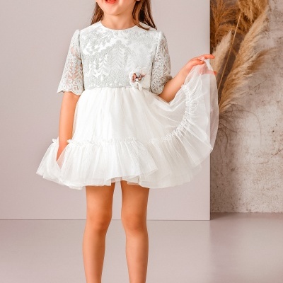 Menina com vestido branco de renda e tule, sapatos brancos, fundo neutro com plantas secas