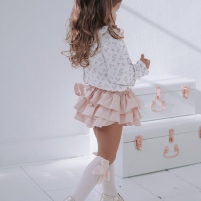 Menina com roupa infantil rosa e branca e sapatos dourados junto a malas brancas.