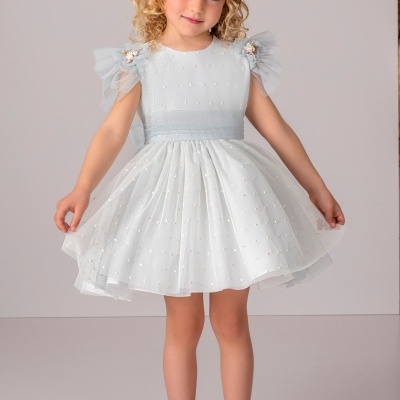 Menina com vestido branco decorado com pérolas e tule, faixa de cabelo florido e sapatos brancos