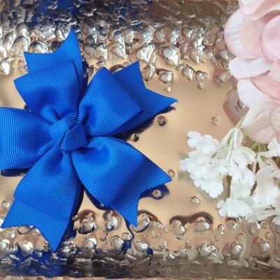 Laço azul de tecido sobre superfície metálica com flores artificiais ao lado