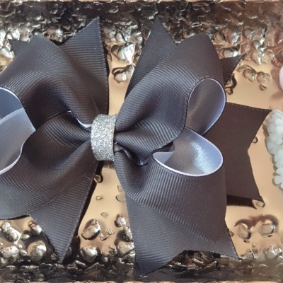 Laço de cabelo cinzento com centro prateado sobre superfície metalizada com flores ao lado