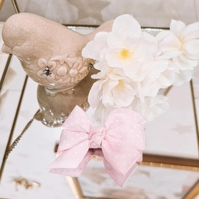 Pássaro decorativo em cerâmica bege com flores artificiais brancas e laço rosa sobre superfície espelhada dourada