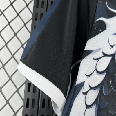Manga de camiseta preta com padrões gráficos em tons de cinza e preto, com detalhes brancos e azul escuro, pendurada num cabide.