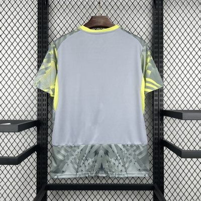 T-shirt desportiva cinza com detalhes amarelos e padrões geométricos, pendurada em estrutura de metal preta com rede