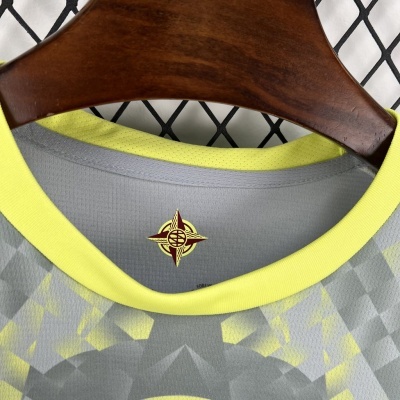 T-shirt cinza com padrão geométrico amarelo e gola amarela pendurada em cabide de madeira