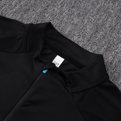 Roupa preta com fecho azul e etiqueta EA7 sobre carpete cinzenta