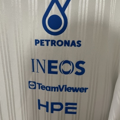 Tecido branco com logótipos azuis de PETRONAS, INEOS, TeamViewer e HPE