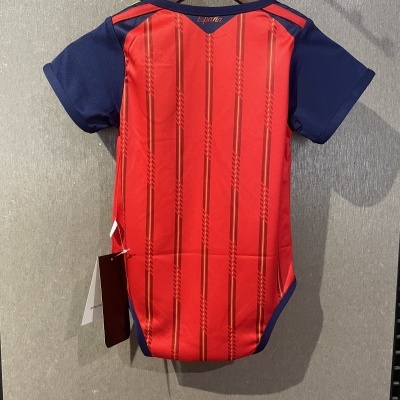 Body de bebé vermelho com riscas amarelas e azuis e mangas azul escuro, pendurado num cabide.