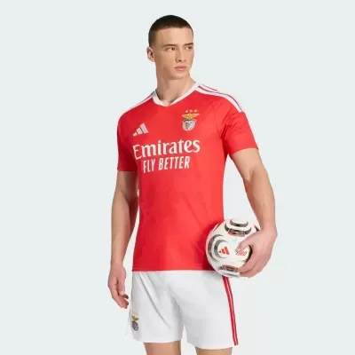 Homem com camisola de futebol vermelha do Benfica e calções brancos segurando bola Adidas
