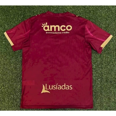 Camisola desportiva vermelha com logos amco e Lusíadas em amarelo sobre relva