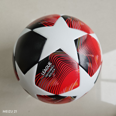 Bola de futebol branca, preta e vermelha com texto LÉAGUE MATCHBALL REPLICA numa superfície clara