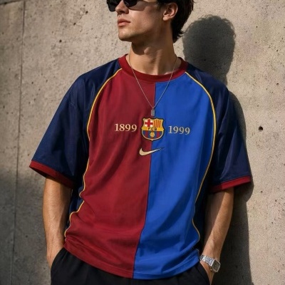 Homem a usar camisa azul e grená do FC Barcelona com logotipo e anos 1899 e 1999, com óculos de sol e relógio, encostado a parede de betão.