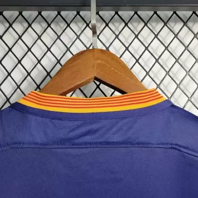 Peça de roupa azul com gola riscada amarela e vermelha num cabide de madeira