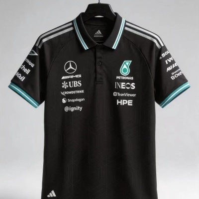 Polo preto com gola com risca verde e branca e vários logótipos de patrocinadores brancos, pendurado num cabide negro