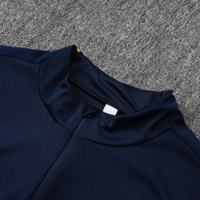 Camisola desportiva azul escuro com fecho, detalhes vermelho e amarelo, logótipo Nike amarelo, sobre tapete cinzento