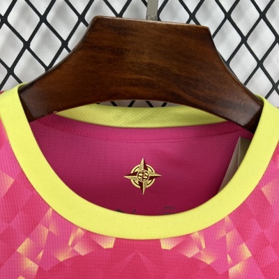 Camisola desportiva rosa e amarela com padrão geométrico num cabide de madeira