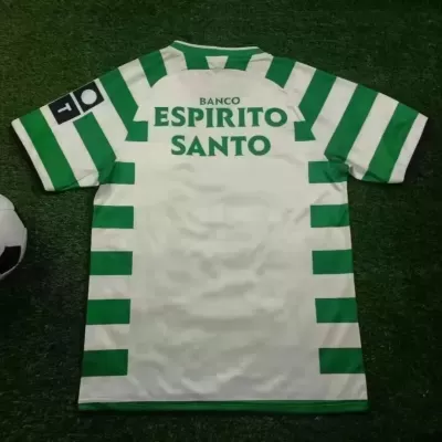 Camisola de futebol branca e verde com texto Banco Espirito Santo nas costas sobre relva com bola ao lado