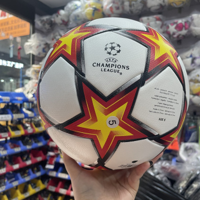 Bola de futebol branca com estrelas coloridas e texto UEFA CHAMPIONS LEAGUE num ambiente de loja