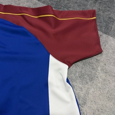 Peça de vestuário azul, branca e burdeos com linha amarela sobre superfície cinza.