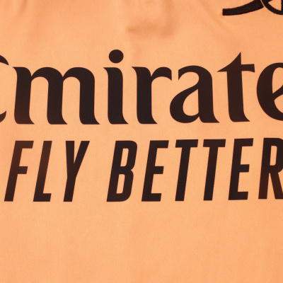 Peça de vestuário cor salmão com texto preto Emirates FLY BETTER