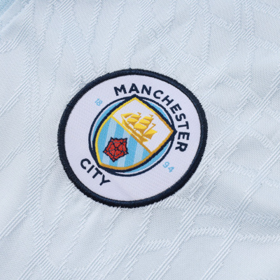 Emblema bordado do Manchester City em tecido azul claro com padrão