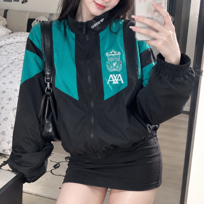Casaco desportivo feminino Adidas preto e verde com logótipo Liverpool FC, feito em tecido leve, combinado com mini saia preta.